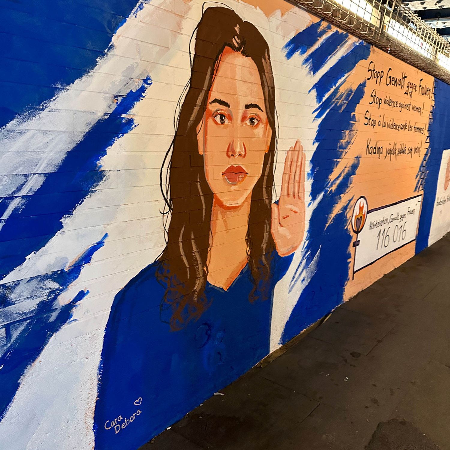Wandmalerei von einer Frau, die mit ihrer Hand Stopp zeigt.